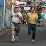 Protagonistas do filme "Balls Up" correndo em uma rua do Brasil durante a copa do mundo.