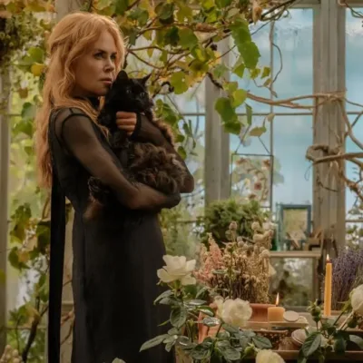 Nicole Kidman como a bruxa Gillian Owens na sequência "Da Magia à Sedução 2". Personagem está com cara fechada, segurando um gato preto no colo com os dois braços, em pé, vista de lado. Ambientação de estufa caseira cheia de plantas.