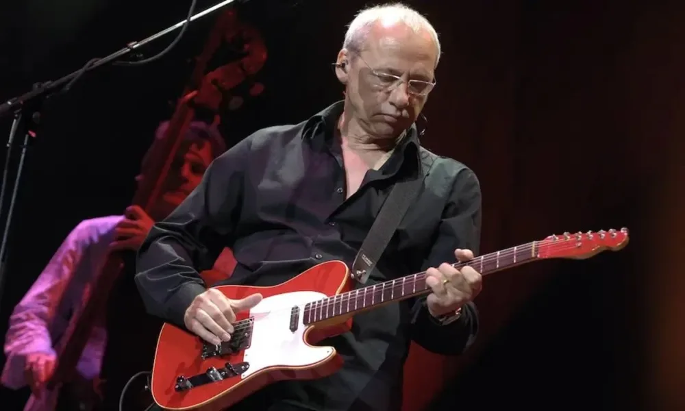 Mark Knopfler durante apresentação da Shangri-La Tour em 2005. Músico está vestido de preto e olhando para sua guitarra.