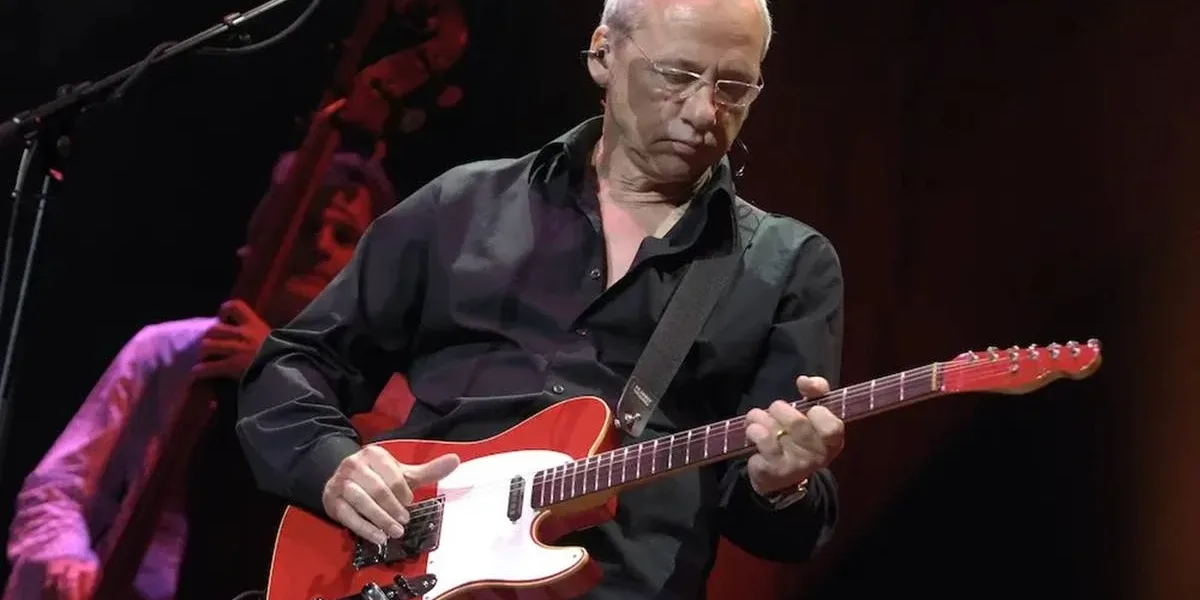 Mark Knopfler durante apresentação da Shangri-La Tour em 2005. Músico está vestido de preto e olhando para sua guitarra.
