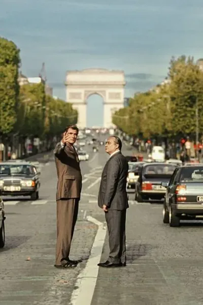 Foto horizontal promocional para o longa "O Grande Arco de Paris", com protagonistas no meio de avenida com Arco do Triunfo atrás. Imagem também é a mesma do pôster.