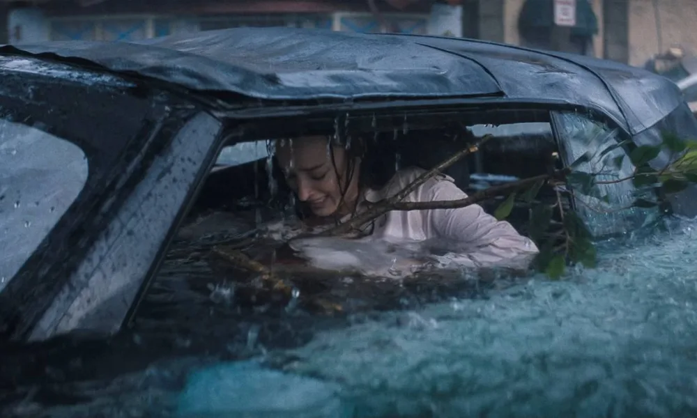 Phoebe Dynevor como Lisa Fields em "Ataque Brutal". Personagem está ensopada dentro de carro, um galho enorme entrando dentro do carro, e ela desesperada.