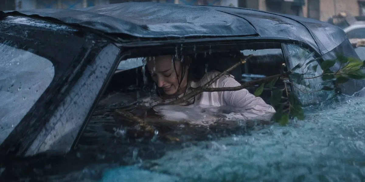 Ataque Brutal | Um Desastre Envolvente Que se Perde no Próprio Absurdo Phoebe Dynevor como Lisa Fields em "Ataque Brutal". Personagem está ensopada dentro de carro, um galho enorme entrando dentro do carro, e ela desesperada.