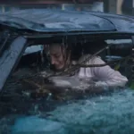 Phoebe Dynevor como Lisa Fields em "Ataque Brutal". Personagem está ensopada dentro de carro, um galho enorme entrando dentro do carro, e ela desesperada.
