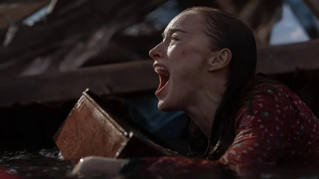 Ataque Brutal | Um Desastre Envolvente Que se Perde no Próprio Absurdo 1 Phoebe Dynevor como Lisa Fields, protagonista de "Ataque Brutal". Ela está ensopada, em escombros, água até o peito e apoiada em uma prancha.