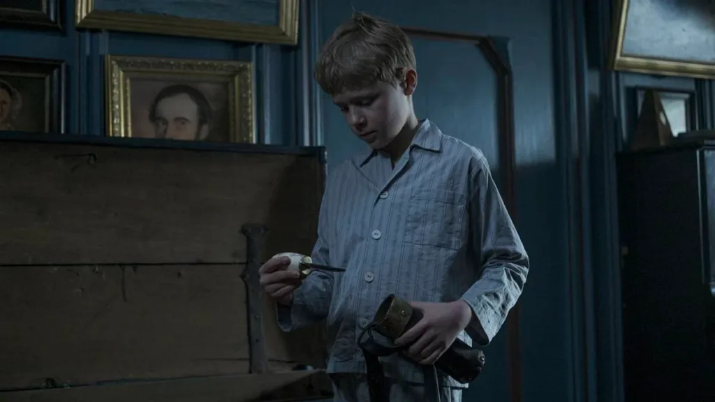 Protagonista de "Uma Infância Alemã", Nanning (Jasper Billerbeck), em cena em quarto escuro com objeto na mão, curioso.