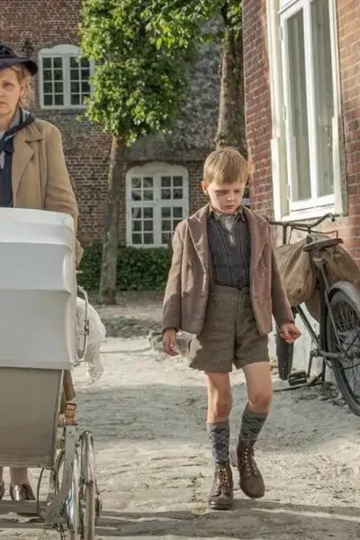 Cena do filme "Uma Infância Alemã". Mãe caminha com dois filhos, um a cada lado, mais o carrinho de bebê que puxa. Ela está com um semblante irritadiço e os garotos cabisbaixos.