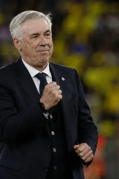 Carlo Ancelotti, técnico da seleção brasileira, punho esquerdo fechado e expressão em sinal de comemoração, terno e gravata em campo durante partida. Imagem gerada por IA.