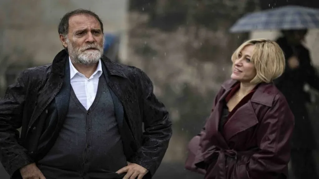 Still do filme "Cinco Segundos" (2025). Valerio Mastandrea como Adriano ao lado de Valeria Bruni Tedeschi como Giuliana. Ela o olha com ele de perfil, ele preocupado com as mãos na cintura.