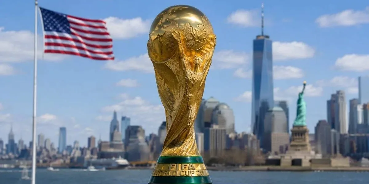 Uma Copa Diferente | Veja Tudo Sobre a Primeira Copa do Mundo com Três Sedes e 48 Seleções Troféu da copa do mundo de futebol com fundo dos EUA com vista de Nova Iorque, bandeira do país tremulando ao fundo.