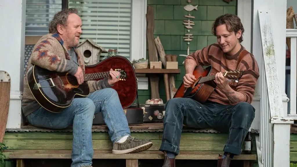 Lewis Pullman e Colm Meaney em "Criaturas Extraordinariamente Brilhantes" como Cameron e Ethan. Eles tocam violão na porta de casa, sentados.