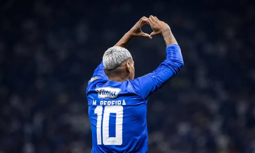 Mateus Pereira, do Cruzeiro, durante partida, fazendo sinal de coração no alto com as mãos. Jogador é visto de costas. Imagem gerada por IA.