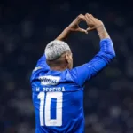 Mateus Pereira, do Cruzeiro, durante partida, fazendo sinal de coração no alto com as mãos. Jogador é visto de costas. Imagem gerada por IA.