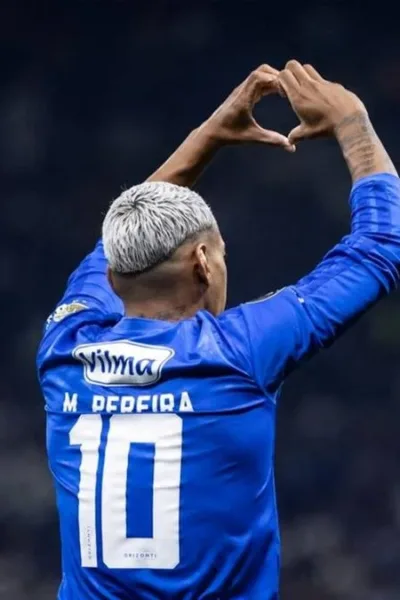 Mateus Pereira, do Cruzeiro, durante partida, fazendo sinal de coração no alto com as mãos. Jogador é visto de costas. Imagem gerada por IA.