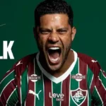 Atacante Hulk em imagem, horizontal, de anúncio de sua vinda para o Fluminense a partir de 2026. Ele está com a camisa do time e dá um grito. Escudo do time está acima de seu nome, à esquerda do fundo verde, gravado em branco.