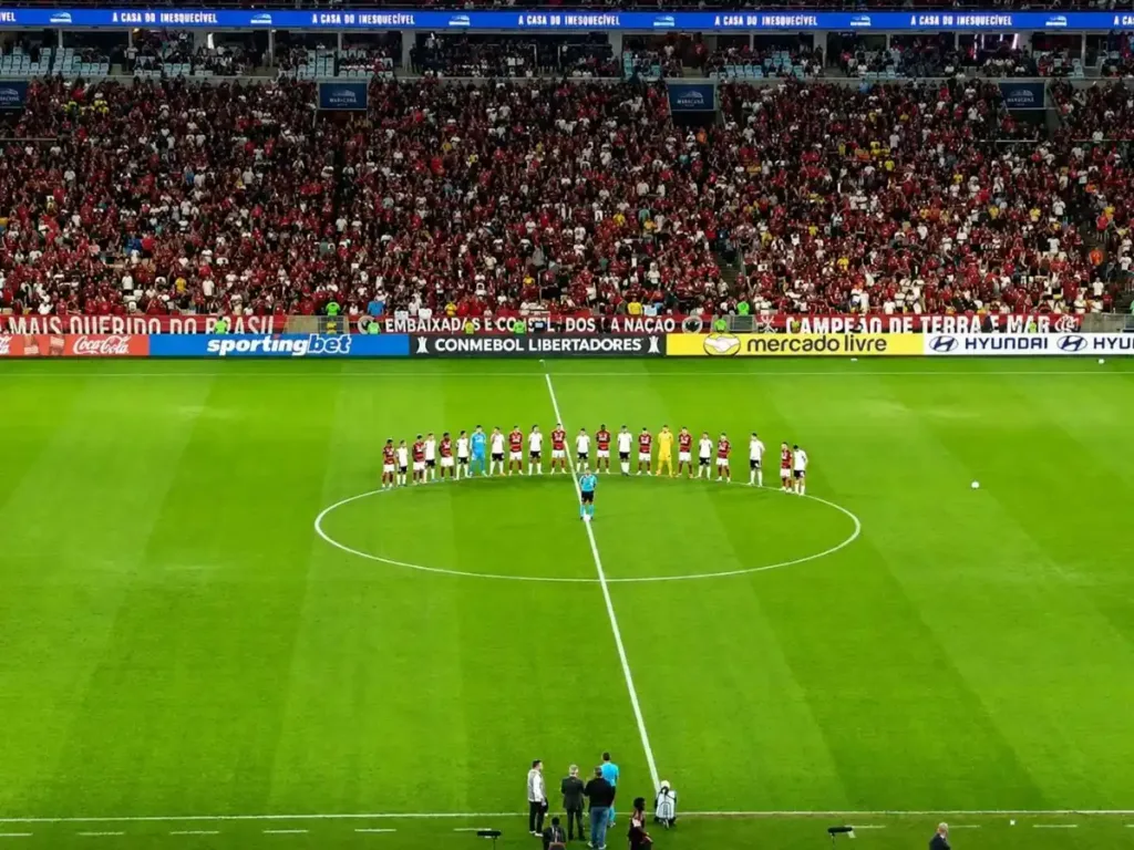 Pedro Decide, Flamengo Vence o Estudiantes e Garante Vaga nas Oitavas da Libertadores 2 Fotografia do jogo Flamengo vs. Estudiantes de La Plata. Jogadores estão em torno do círculo central.