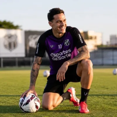 Jogador do Ceará FC ajoelhado apoiado sobre um dos joelhos, sorrindo, olhando de canto, fim de tarde, segurando bola com mão direita. Imagem gerada por IA.