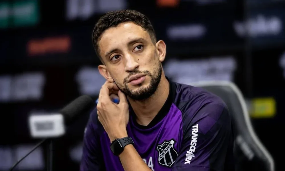 Júlio César, do Ceará, em coletiva de imprensa respondendo pergunta, com mão levada para perto do queixo. Imagem gerada por IA.