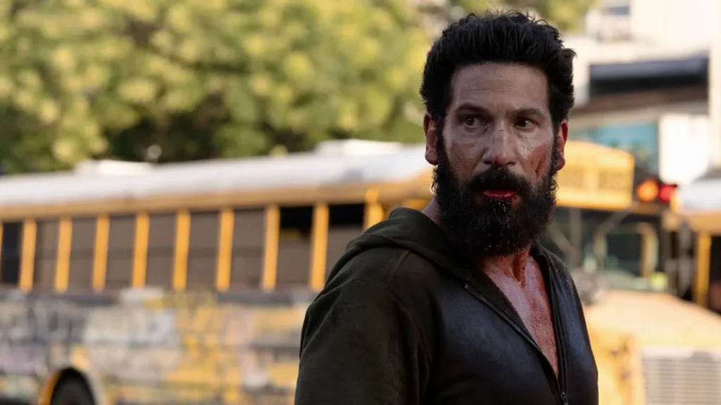 O Justiceiro: Uma Última Morte | Justiceiro Retorna ao Caos e aos Próprios Fantasmas em Especial 3 Jon Bernthal como Frank Castle em "Justiceiro: Uma Última Morte". Semblante de preocupação, corpo levemente virado, paisagem diurna clara contrastando com suas roupas e maquiagem soturna.