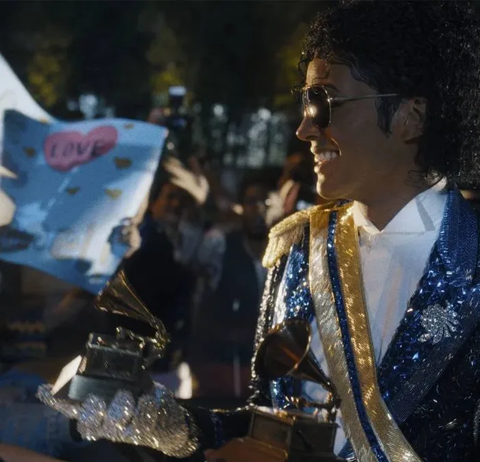 Jaafar Jackson caracterizado como seu tio, Michael Jackson, no filme biográfico "Michael", ele está com uma roupa brilhante azul de baile com ombreira, óculos escuros, segurando dois prêmios Grammy.