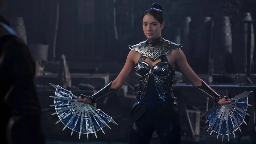 Esta imagem mostra a atriz Adeline Rudolph no papel da personagem Kitana em Mortal Kombat II. Postura séria, um leque em cada mão, em posição de guarda, braços abertos.