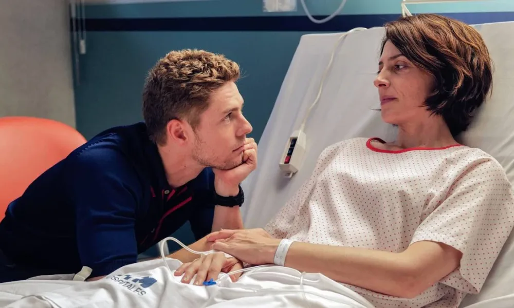 Esta imagem mostra uma cena do filme "Amarga Navidad", dirigido por Pedro Almodóvar. A protagonista está em um leito de hospital olhando para um homem que a olha ternamente, com queixo apoiado na mão esquerda.