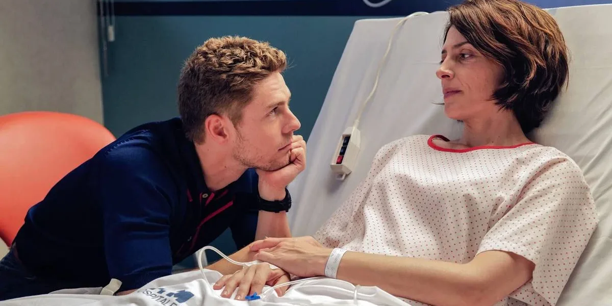 Natal Amargo | Pedro Almodóvar Faz Autoficção Sobre Ego, Luto e Bloqueio Criativo Esta imagem mostra uma cena do filme "Amarga Navidad", dirigido por Pedro Almodóvar. A protagonista está em um leito de hospital olhando para um homem que a olha ternamente, com queixo apoiado na mão esquerda.