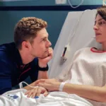 Esta imagem mostra uma cena do filme "Amarga Navidad", dirigido por Pedro Almodóvar. A protagonista está em um leito de hospital olhando para um homem que a olha ternamente, com queixo apoiado na mão esquerda.