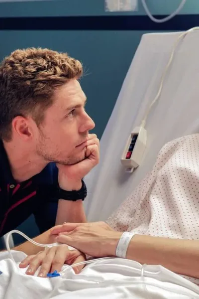 Natal Amargo | Pedro Almodóvar Faz Autoficção Sobre Ego, Luto e Bloqueio Criativo Esta imagem mostra uma cena do filme "Amarga Navidad", dirigido por Pedro Almodóvar. A protagonista está em um leito de hospital olhando para um homem que a olha ternamente, com queixo apoiado na mão esquerda.