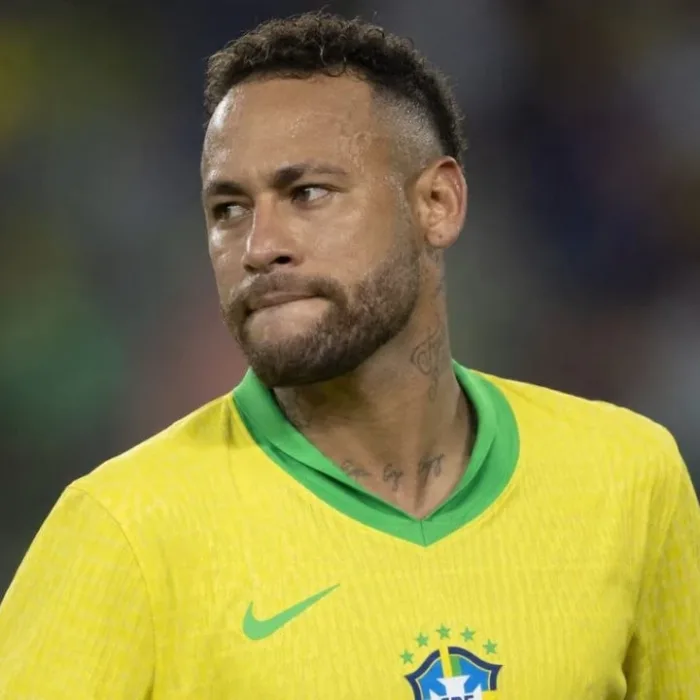 Neymar, rosto virado, lábios para dentro, expressão neutra, durante partida, fundo embaçado de audiência em estado. Ele está com camisa da seleção brasileira. Imagem gerada por IA.