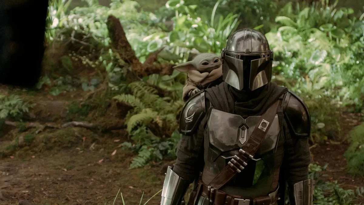 O Mandaloriano e Grogu | Filme Resgata a Essência Clássica de Star Wars nos Cinemas 3 O Mandaloriano, na metade direita da tela, em uma paisagem de floresta, com Grogu no ombro. Imagem de "O Mandaloriano e Grogu".