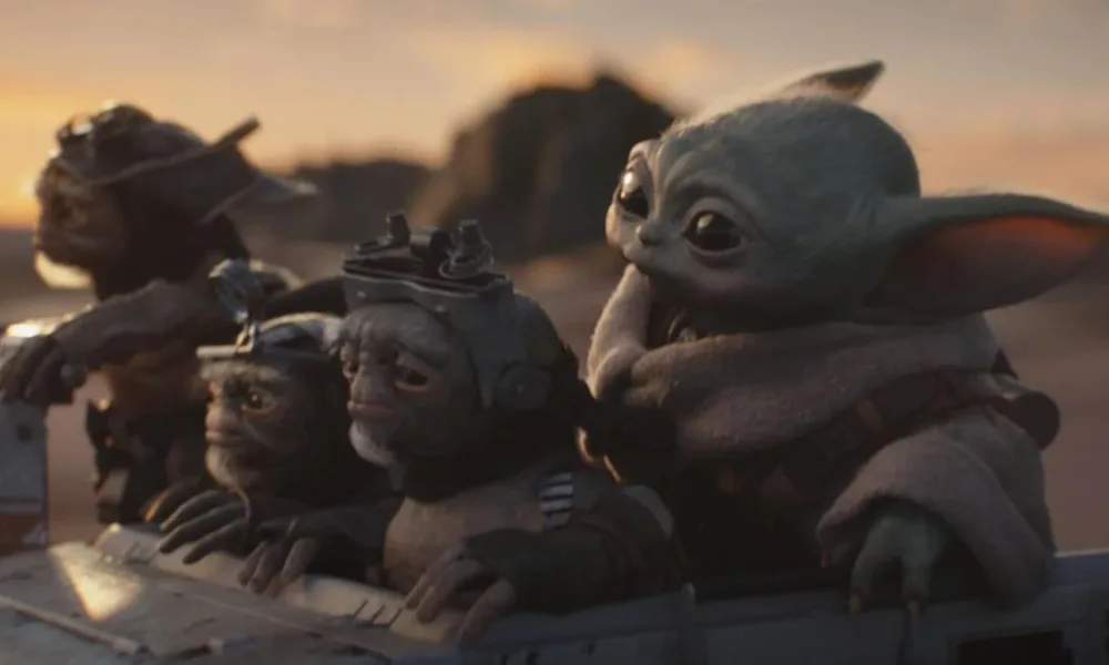 Grogu cercado de outros alienígenas em "O Mandaloriano e Grogu" em um fundo de fim de tarde numa paisagem desértica do filme "Mandaloriano e Grogu".