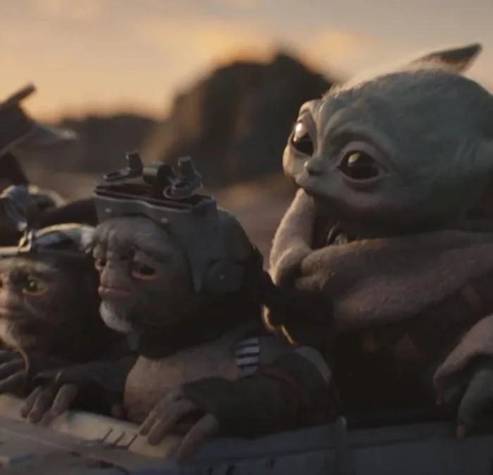 Grogu cercado de outros alienígenas em "O Mandaloriano e Grogu" em um fundo de fim de tarde numa paisagem desértica do filme "Mandaloriano e Grogu".