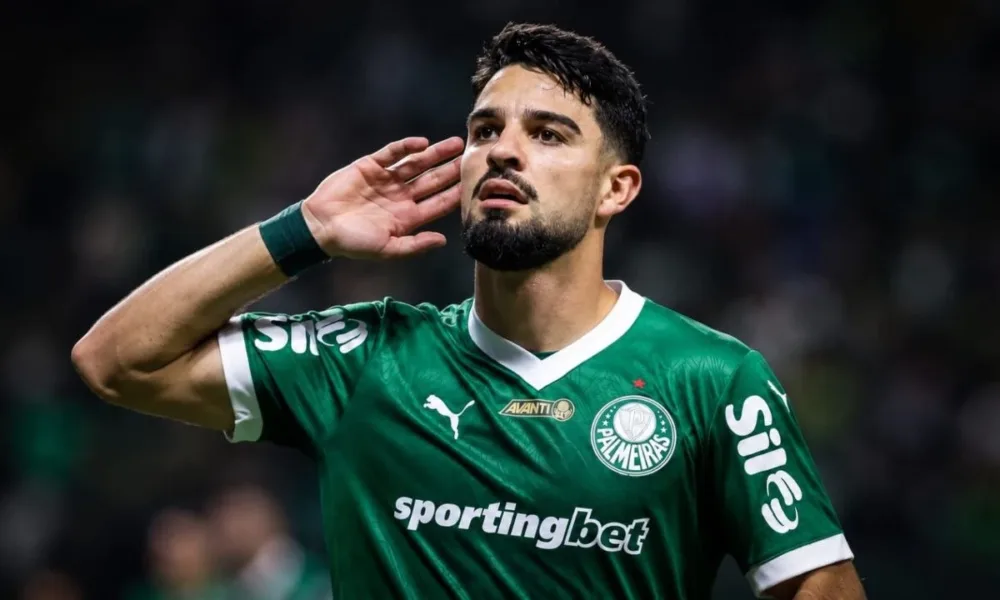 Esta imagem mostra o atacante argentino José Manuel "Flaco" López, que atualmente joga pelo Palmeiras. Ele leva a mão esquerda à orelha. Imagem gerada por IA.