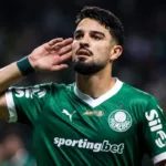 Esta imagem mostra o atacante argentino José Manuel "Flaco" López, que atualmente joga pelo Palmeiras. Ele leva a mão esquerda à orelha. Imagem gerada por IA.