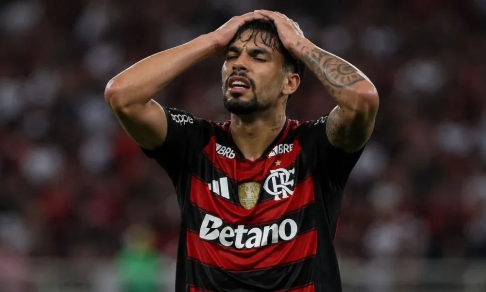 Esta imagem mostra Lucas Paquetá vestindo a camisa do Flamengo. Ele leva as mãos à cabeça em desespero. Imagem gerada por IA.