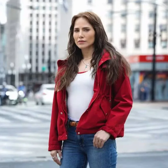 Letícia Collin como personagem protagonista da nova novela das 9, "Quem Ama Cuida". Ela está de jaqueta vermelha e uma paisagem urbana de São Paulo ao fundo.
