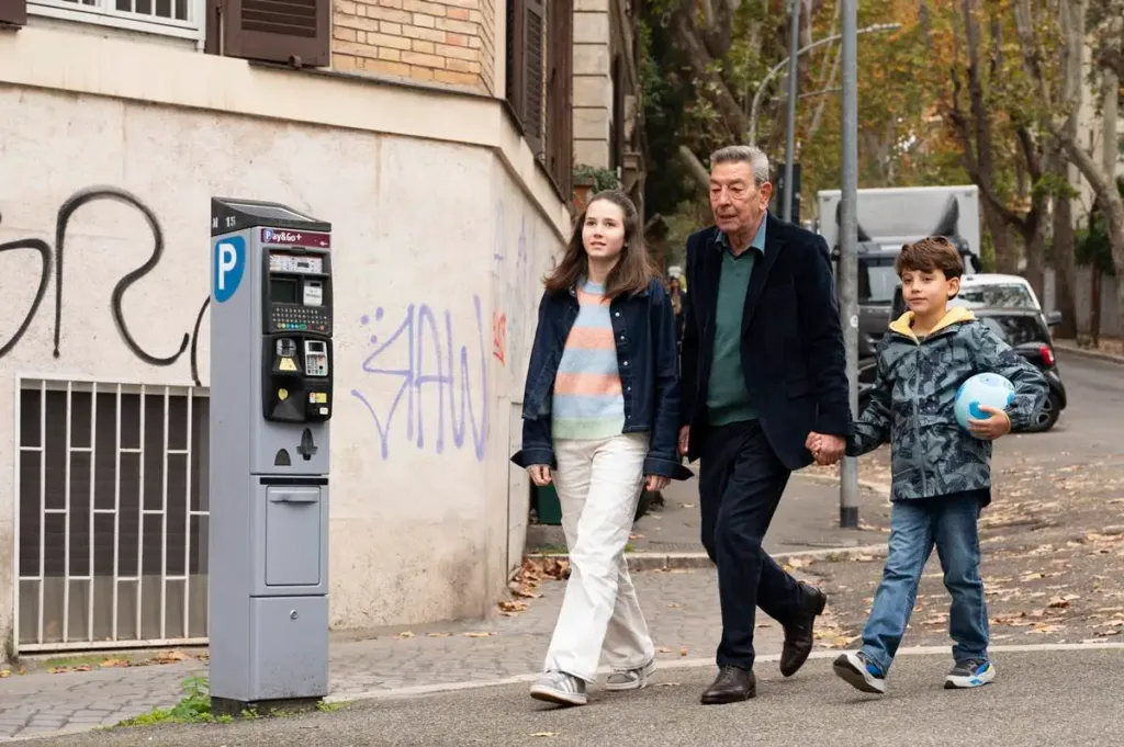 Still do filme "Querendo Ou Não", 2025. Professor anda com duas parentes crianças.