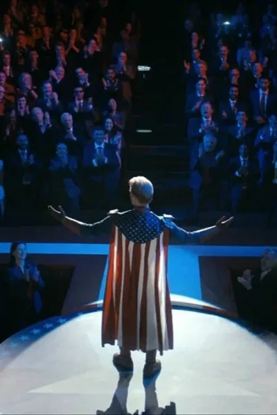 Homelander em um ambiente escuro iluminado apenas no palco, com ele em destaque, braços abertos, uma multidão em um nível abaixo, majoritariamente masculina, aplaudindo eufórica. Imagem do 1º episódio da 5ª temporada de "The Boys".