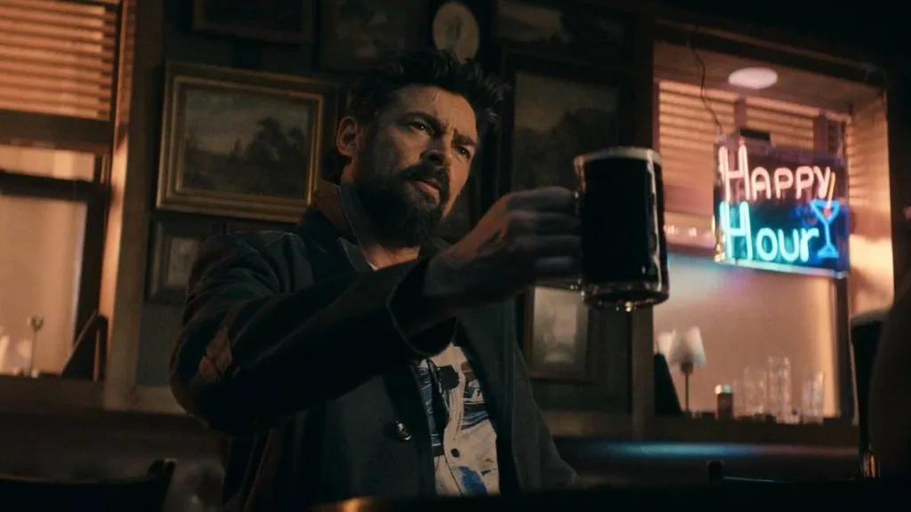 The Boys (5ª Temporada) | Entre Acertos e Excessos, Série Encerra Sua História, Com Desempenho Abaixo do Esperado 2 Karl Urban como Billy Butcher no episódio 3 da 5ª temporada de "The Boys". Sentado, levanta um copo em comemoração, uma expressão séria no rosto.