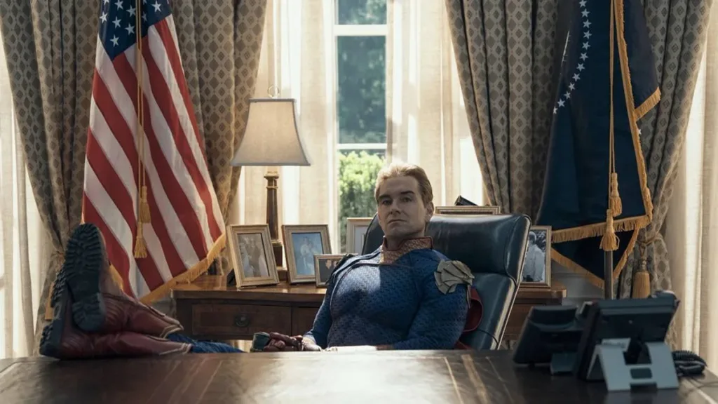 Antony Starr como o Homelander no 7º episódio da 5ª temporada de The Boys. Ele está com os pés sobre a mesa, bandeira dos EUA ao fundo, uma expressão inquieta.