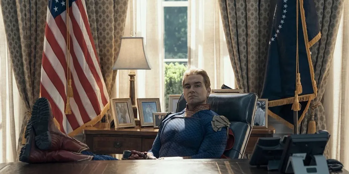 The Boys (5ª Temporada) | Entre Acertos e Excessos, Série Encerra Sua História, Com Desempenho Abaixo do Esperado Antony Starr como o Homelander no 7º episódio da 5ª temporada de The Boys. Ele está com os pés sobre a mesa, bandeira dos EUA ao fundo, uma expressão inquieta.