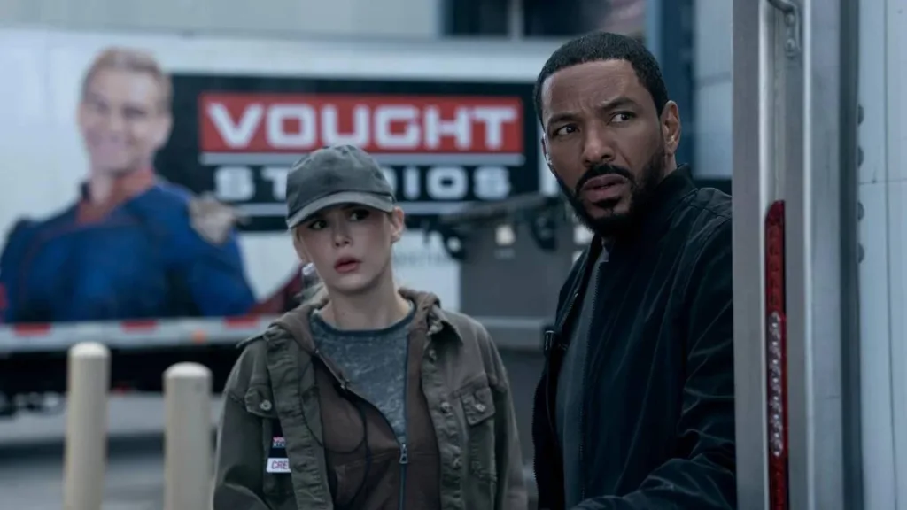 Esta imagem mostra uma cena da quinta e última temporada da série The Boys, produzida pela Amazon Prime Video. O ator Laz Alonso interpreta Marvin T. Milk, também conhecido como Leitinho (Mother's Milk). A personagem ao lado dele é a Annie January, interpretada por Erin Moriarty. Ao fundo, vê-se um caminhão da Vought Studios, a corporação que controla os super-heróis da série.