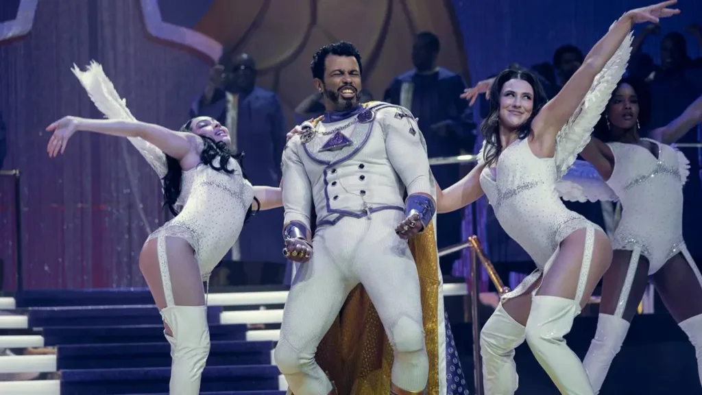 Esta imagem mostra o ator Daveed Diggs interpretando o personagem "Oh Father" na série The Boys. A cena é um número musical do sétimo episódio da quinta temporada da série.