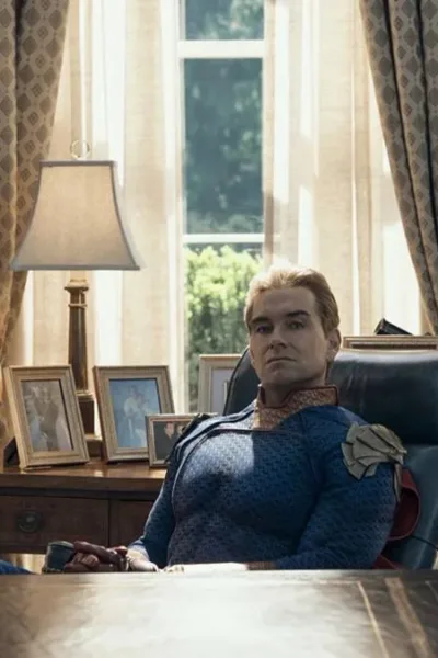 Antony Starr como o Homelander no 7º episódio da 5ª temporada de The Boys. Ele está com os pés sobre a mesa, bandeira dos EUA ao fundo, uma expressão inquieta.