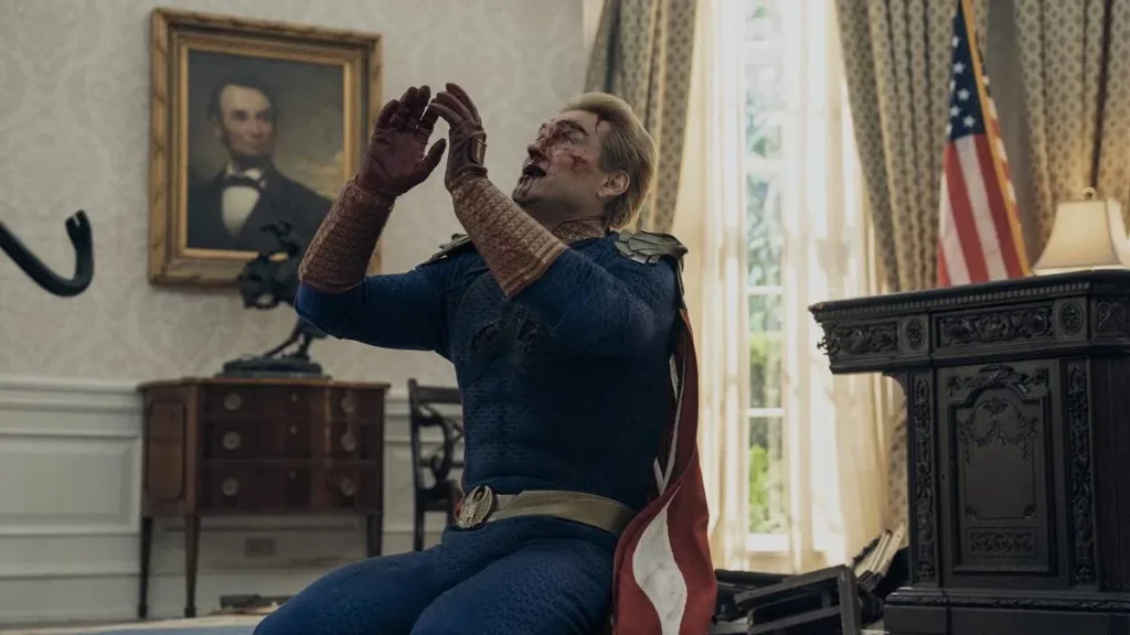 Esta imagem mostra Antony Starr como o Capitão Pátria na 5ª temporada de The Boys. A cena retrata um momento crítico no final da série, onde o personagem principal é mostrado enfraquecido, pé de cabra no canto esquerdo da tela e ele implorando pela vida, de joelhos.