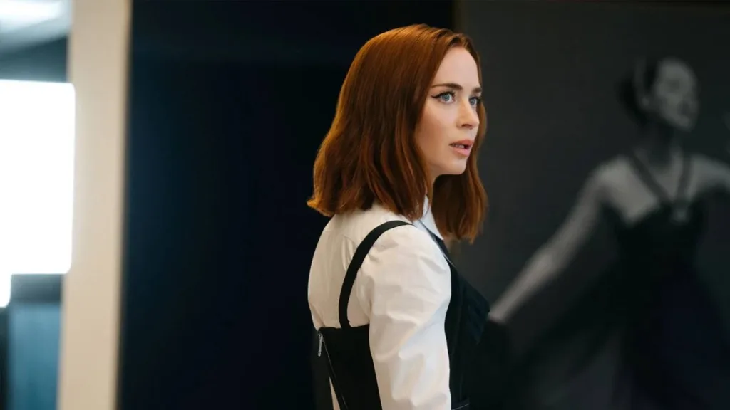 Emily Blunt como Emily Charlton em "O Diabo Veste Prada 2", vista de perfil, rosto com expressão de leve surpresa.