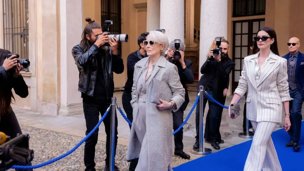 Meryl Streep como Miranda Priestly em "O Diabo Veste Prada 2" seguida por sua equipe e sendo fotografada por paparazzi.
