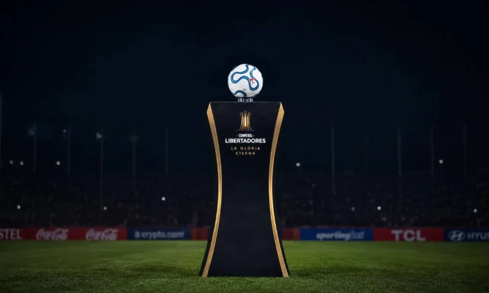 Troféu da Copa Libertadores sobre estande sobre o gramado de noite. Imagem gerada por IA.