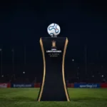 Troféu da Copa Libertadores sobre estande sobre o gramado de noite. Imagem gerada por IA.